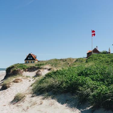 VisitDenmark_North_Jutland_Skagen_House at the beach with a waving Danish flag